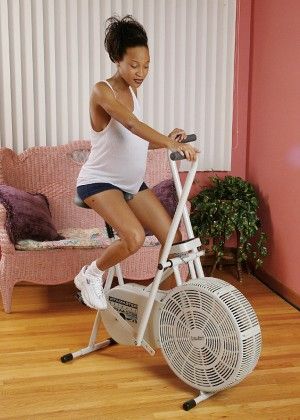 A pregnant black woman undressed on a stationary bike